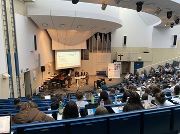 Menschen sitzen in einem Universitätssaal und blicken auf eine Gesprächsrunde.