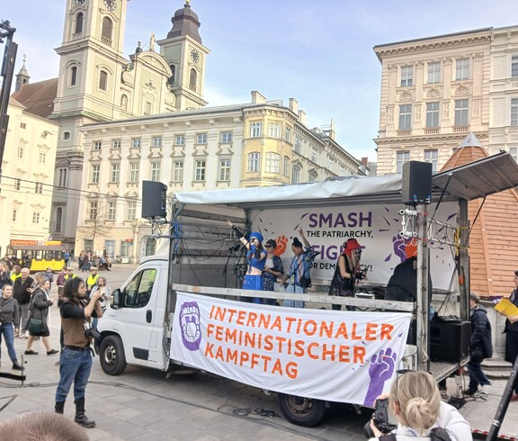 Ein offener Wagen mit einem großen Banner zum Internationalen Feministischen Kampftag am Hauptplaz in Linz. 