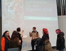 Sechs Menschen diskutieren vor einer Videowand.