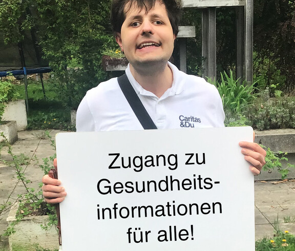 Ein Mann hält ein Schild in der Hand auf dem steht "Zugang für Gesundheitsinformationen für alle"