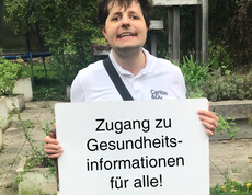 Ein Mann hält ein Schild in der Hand auf dem steht "Zugang für Gesundheitsinformationen für alle"