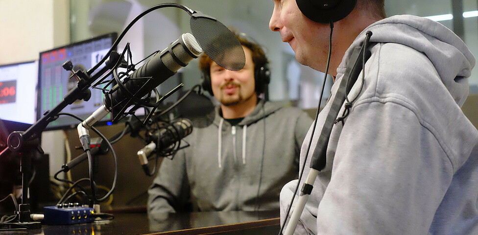 Zwei Männer sitzen in einem Aufnahmestudio. 