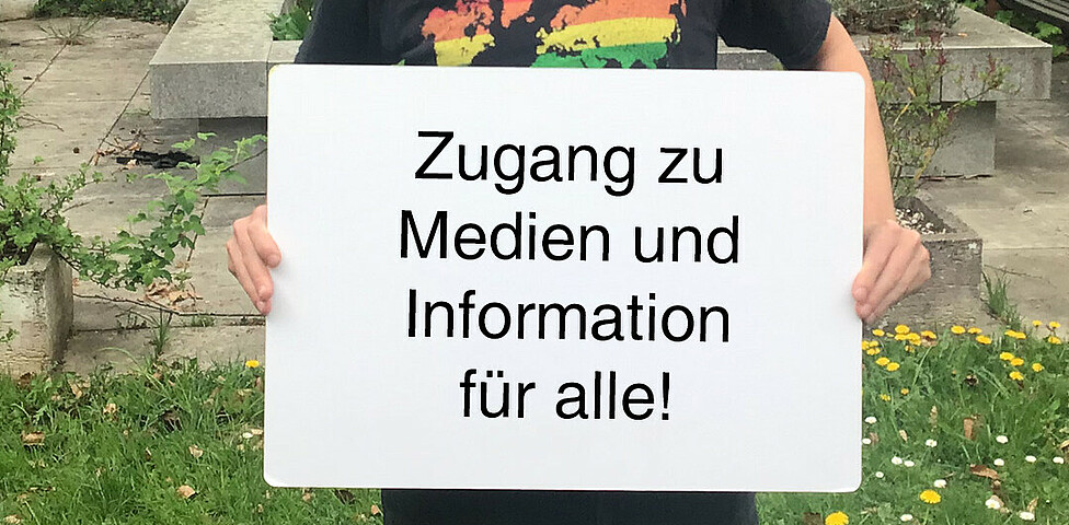 Ein Mann hält ein Schild in der Hand auf dem steht "Zugang zu Medien und Information für alle"